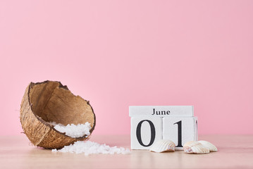Wooden block calendar with date June 1 and coconut with sea salt on the pink background. Summer vacation concept