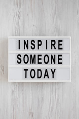 'Inspire someone today' words on a modern board on a white wooden background, top view. Overhead, from above, flat lay. Close-up.