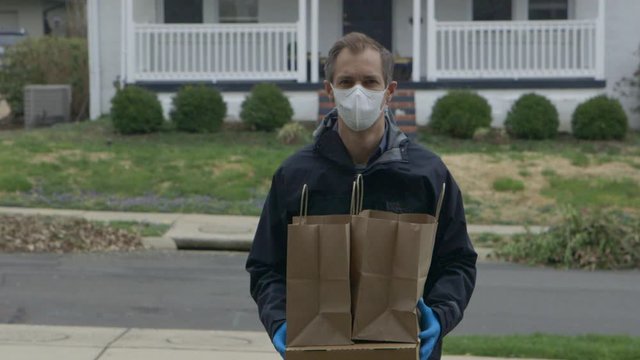 A delivery man wearing a medical mask and gloves delivers goods to a house.