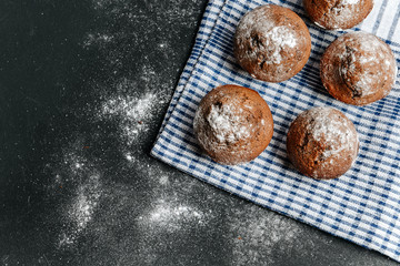 Obraz na płótnie Canvas Chocolate muffins and a checkered napkin lie on a black table sprinkled with flour.