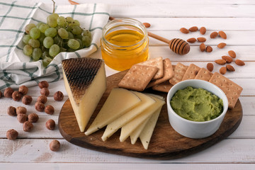 Cheese served with grapes, guacamole, honey, crackers and nuts on a light wooden background.