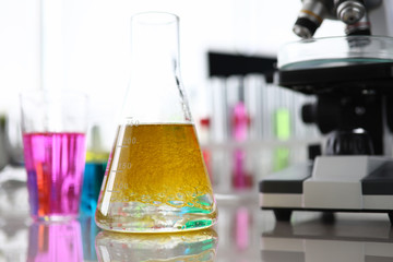 Close-up of laboratory tube with yellow liquor, microscope. Biotechnology investigation and pharmacy manufacturing. Chemistry industry and lab research concept