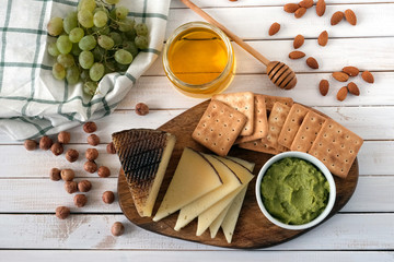 Cheese served with grapes, guacamole, honey, crackers and nuts on a light wooden background. Top view