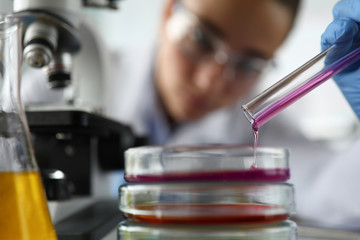 Close-up of laboratory assistant pouring reagent in test container. Researcher investigating liquid...