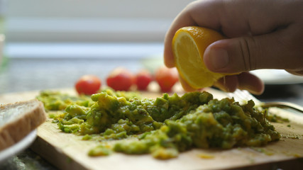 Close up Of Hand Squeezes Lemon Juice Over Avocado Toast. Breakfast Time, Healthy Food.