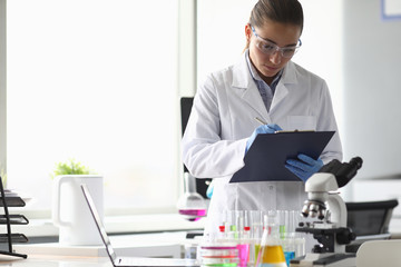 Portrait of concentrated woman looking at documents with seriousness. Lab assistant writing results...