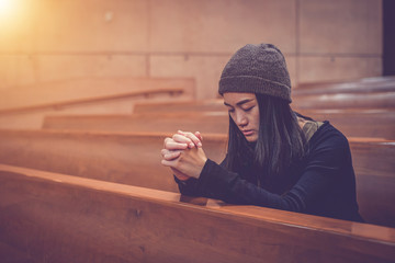 Young woman prayer's pray alone in church, People pray to God with folded hands, old wooden classic long chairs background