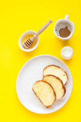 Homemade sweet bread with honey on a plate and a cup of coffee. Breakfast. Yellow paper background. Top view.