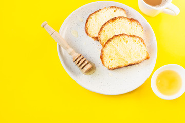 Homemade sweet bread with honey on a plate and a cup of coffee. Breakfast. Yellow paper background. Top view.