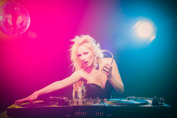 Beautiful blonde DJ girl in a white suit on decks on the party on the black background