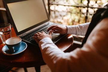 
A young businessman sits in a cafe and works at a computer. A computer and a cup of coffee