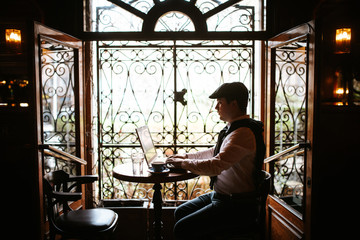 
A young businessman sits in a cafe and works at a computer. Business man working and sitting by window