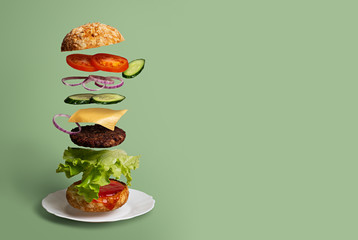 Delicious Burger with flying ingredients on a light green background. Concept of food levitation...