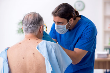 Fototapeta premium Old man visiting young male doctor dermatologist