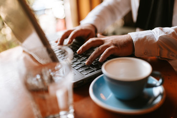 
A young businessman sits in a cafe and works at a computer. A computer and a cup of coffee