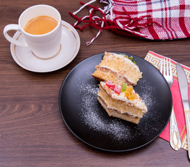 Cake on a black plate, with a mug of coffee, cutlery on the table
