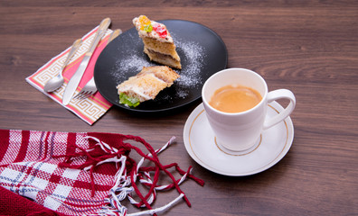 Cake on a black plate, with a mug of coffee, cutlery on the table