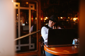 
A young caucasian handsome businessman sits in a cafe talking on the phone in front of a laptop