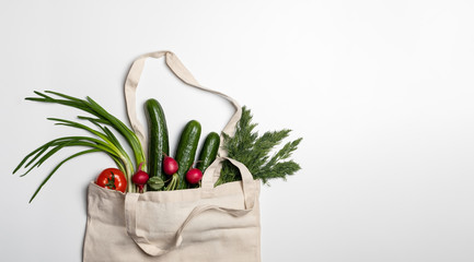 Fresh vegetables and herbs in a string bag made of natural materials, eco-friendly product on a light gray background copy-space. No plastic