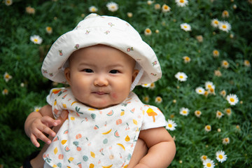 Fat pretty Asian baby infant smiling in background of flowers garden.