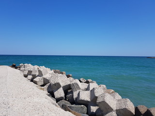 Fototapeta na wymiar Pier of the town of Pomorie / Bulgaria, covered with breakwaters around, which protects the beach and the city from strong waves. Beautiful view during summer time vacation of Black Sea.