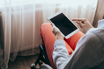 unrecognizable young disabled woman in a wheelchair with a modern tablet.