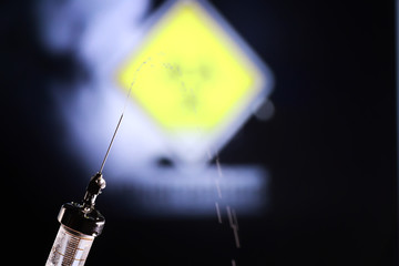 Medical syringe with a needle and a cure for the virus. A drop of drug flows down the needle....