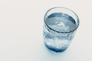 glass of water with ice cubes on a light background.