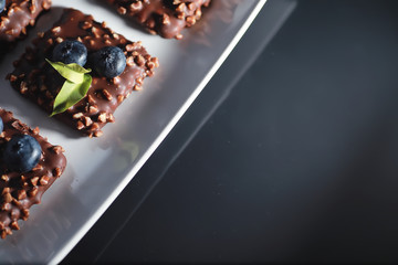 Chocolate dessert with nuts and fresh berries. Sweet snack for coffee biscuit in glaze and nut crumbs with fruit.