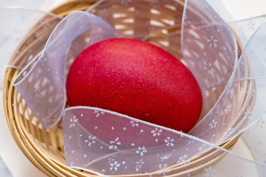 A red painted Easter egg lies in a wicker basket