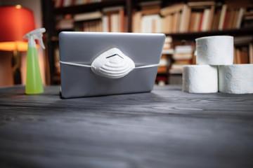 Laptop with protective antiviral mask, chemical spray for decontamination and a stock of toilet paper for the days od pandemic.