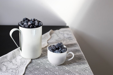Two aluminum and porcelain cups with honeysuckle are on the table. Still life.