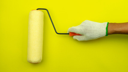 Hand holding painting wall with a paint roller on yellow wall.