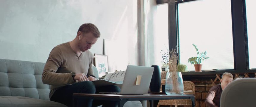Mid 30s Caucasian male working from home, having a video call with colleagues. Family playing in the background. Stay home, quarantine remote work. Shot on RED Dragon