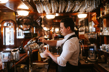 A young caucasian waiter pours beer at a bar