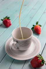 White coffee Cup on a turquoise wooden table. Strawberries in still life. The milk pours into the Cup. A stream of cream.