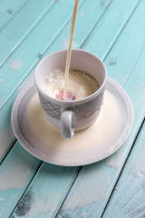 White coffee Cup on a turquoise wooden table. Strawberries in still life. The milk pours into the Cup. A stream of cream.