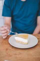 Obraz na płótnie Canvas Man wear blue t-shirt sitting in coffee shop eating lemon cheesecake in white plate with folk.Tasty fresh homemade cream cheese sweet cake for breakfast.Eat delicious dessert is good for your mood. 