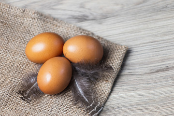 Three brown eggs with feathers on the sacking.Eggs on a wooden background