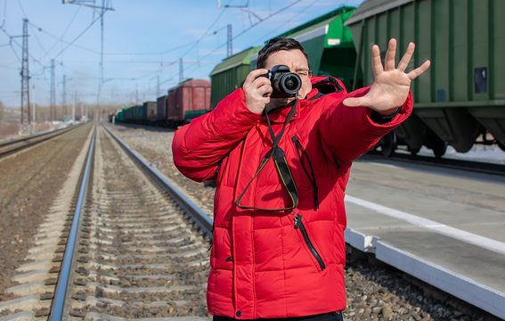 a guy, an oddball with a camera takes a picture of his hand, stops the train while standing on the tracks at the railway station