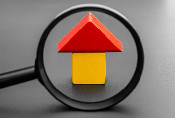 House from toy blocks with magnifying glass on black. Searching or checking house.