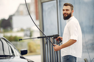 Man in a white shirt. Male washing a car. Guy spray a water