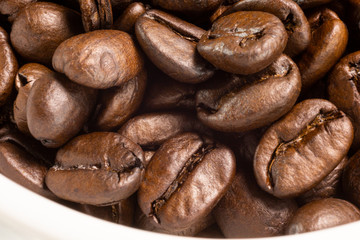 A macro closeup view of dark roasted coffee beans on a table surface.