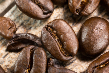 A macro closeup view of dark roasted coffee beans on a table surface.