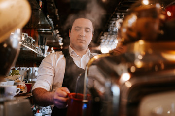
A young caucasian waiter makes coffee in a cafe