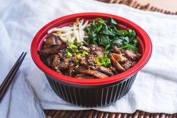 A view of a grilled beef rice bowl, in a restaurant or kitchen setting.
