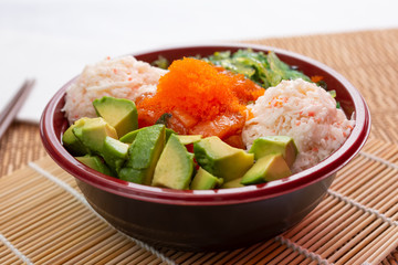 A view of a poke bowl with imitation crab meat, avocado and flying fish roe, in a restaurant or kitchen setting.