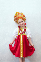 Child girl in Russian national costume sundress and kokoshnik. A child stands against a light wall. National traditions and culture