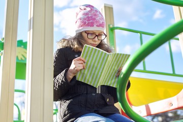 Smart child girl, 8-9 years old, in jacket hat glasses, reading book