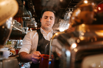 
A young caucasian waiter makes coffee in a cafe